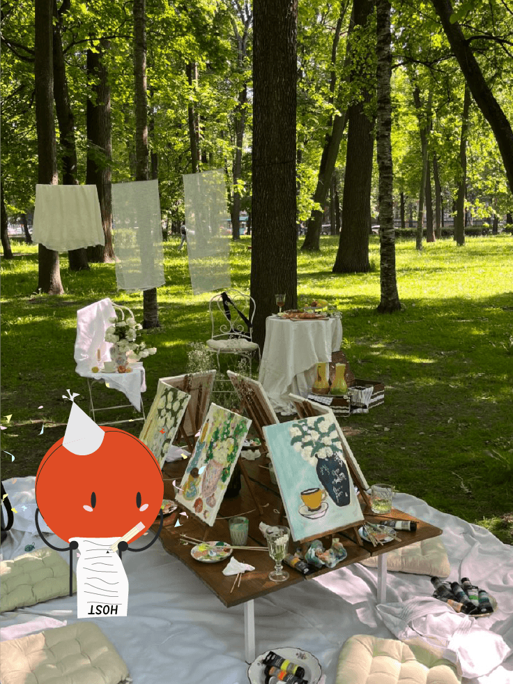 A Nuclii host preparing a paint and sip beneath park trees with easels, canvases and a table ready for guests